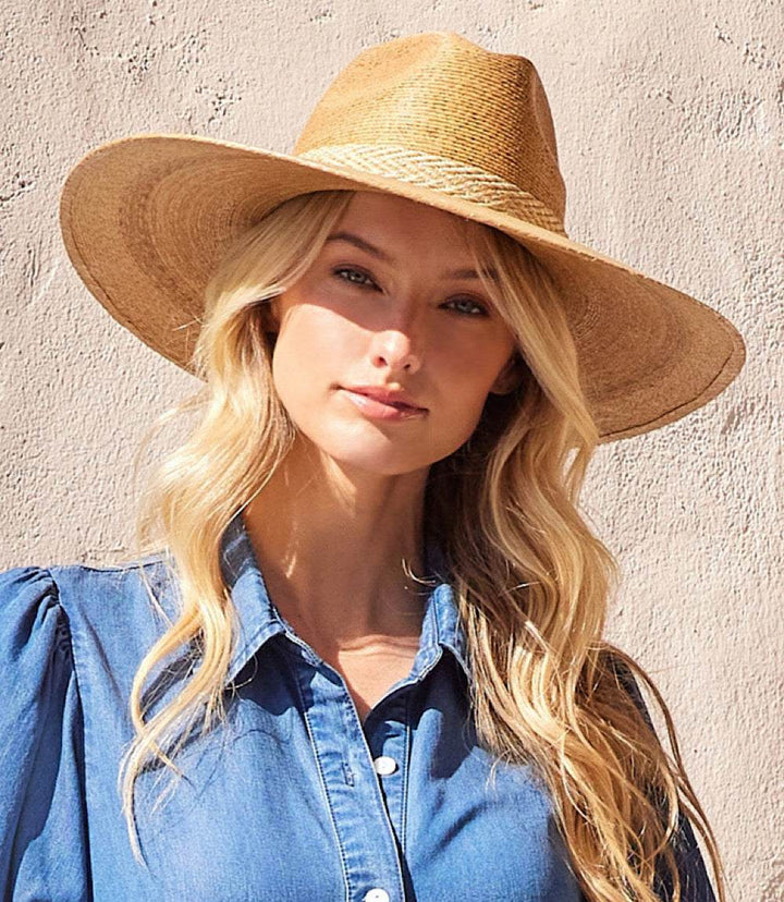 Woman wearing a wide brim palm leaf hat with braided cotton trim and denim shirt