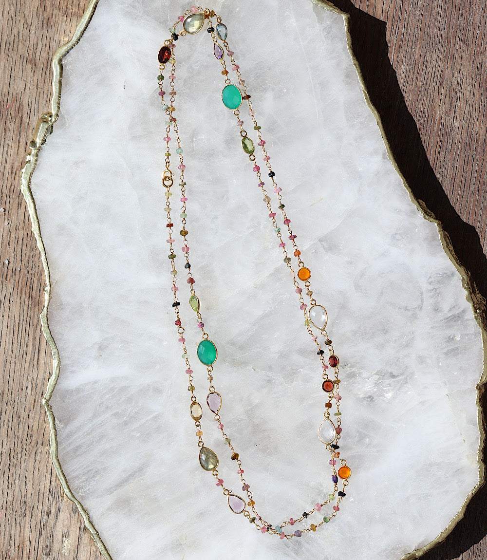 Multi color beaded necklace with tourmaline gemstones and gold plated sterling silver chain on white stone background