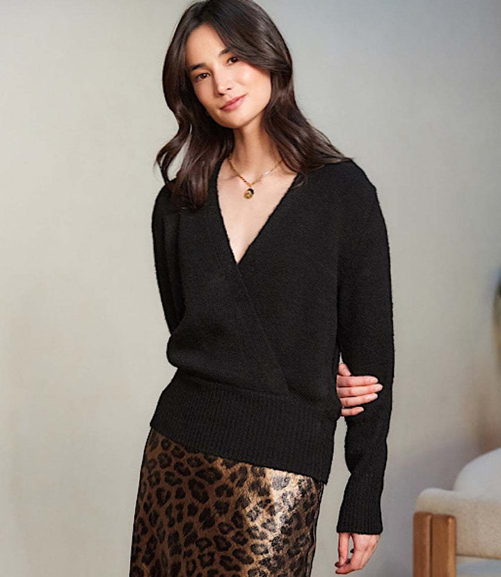 Woman wearing a black wrap sweater with crossover V-neck and drop shoulder sleeves paired with a leopard print skirt