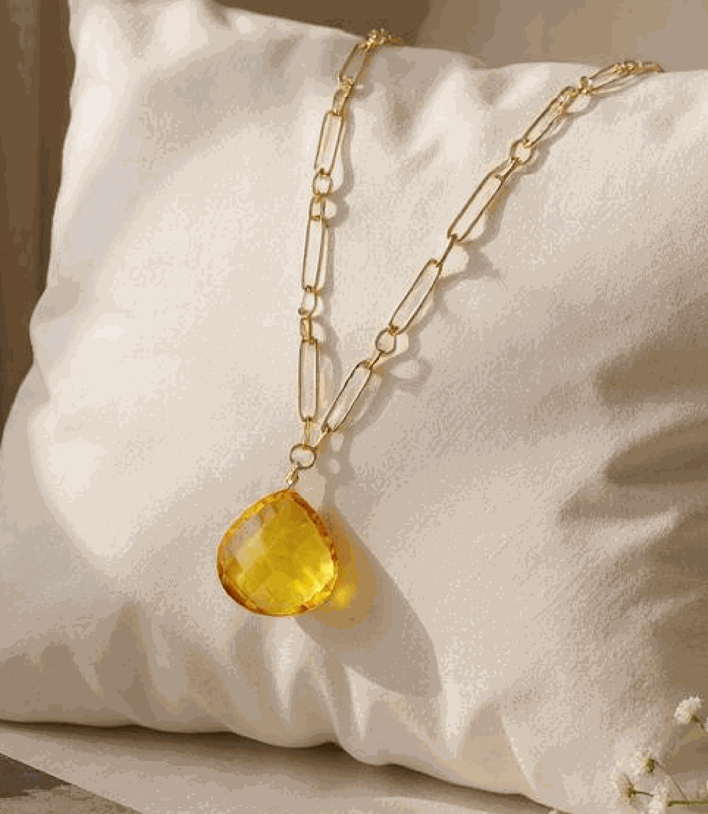 Faceted citrine quartz pendant on gold plated brass chain displayed on white cushion