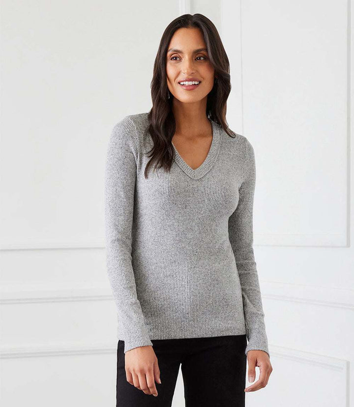 Woman wearing a grey long sleeve ribbed V-neck top with a fitted, stretchy design and set-in sleeves.