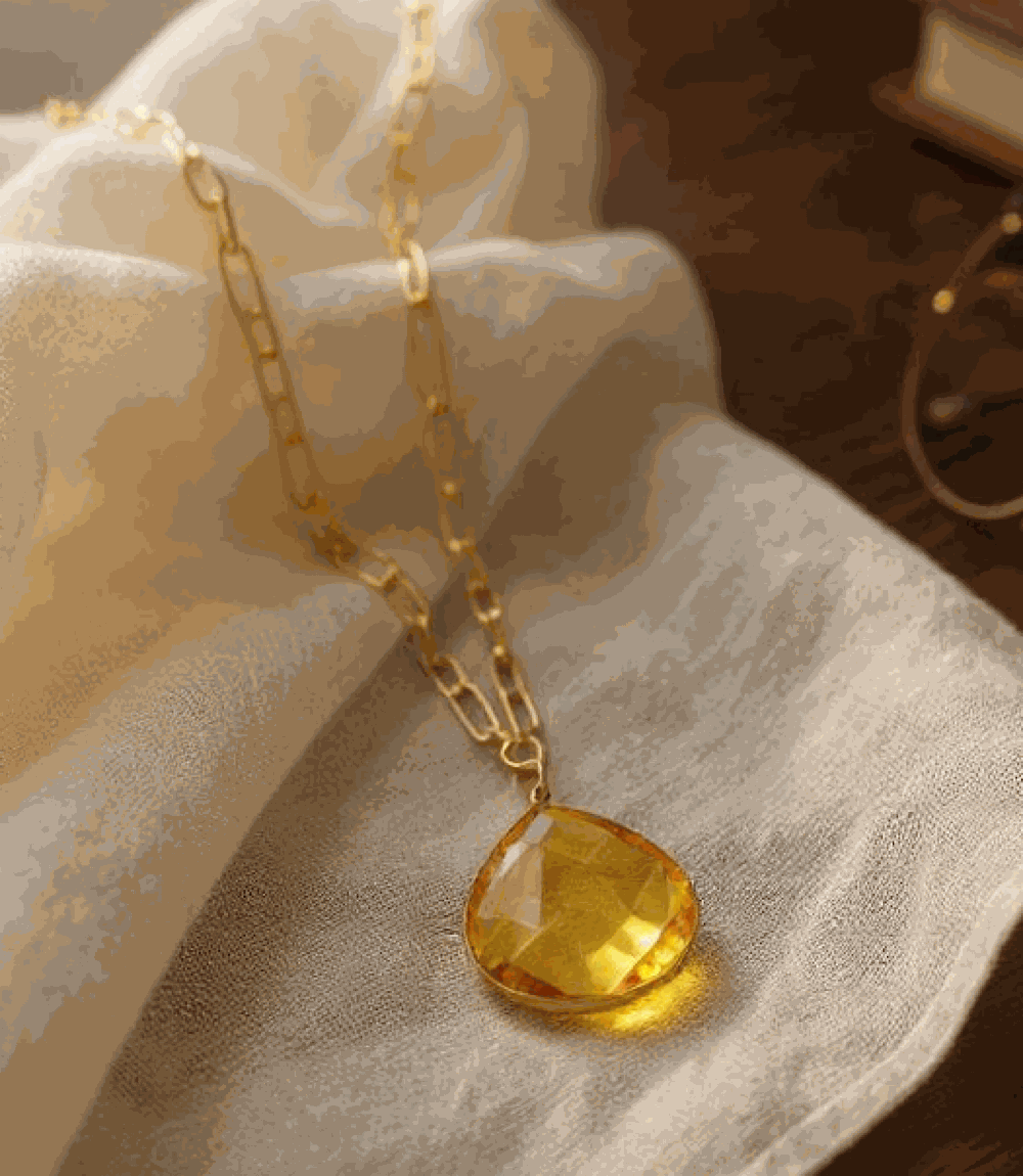 Faceted citrine quartz pendant necklace with gold-plated brass chain on fabric background