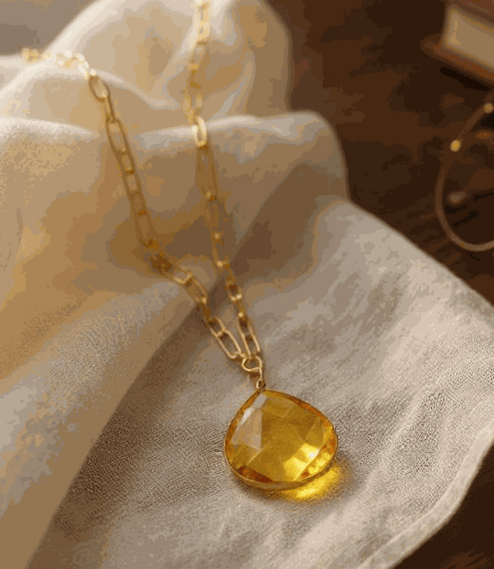 Faceted citrine quartz pendant necklace with gold-plated brass chain on fabric background