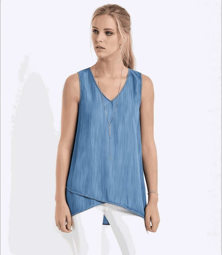 Woman wearing blue asymmetric tank top with crossover hem and V-neckline paired with white pants