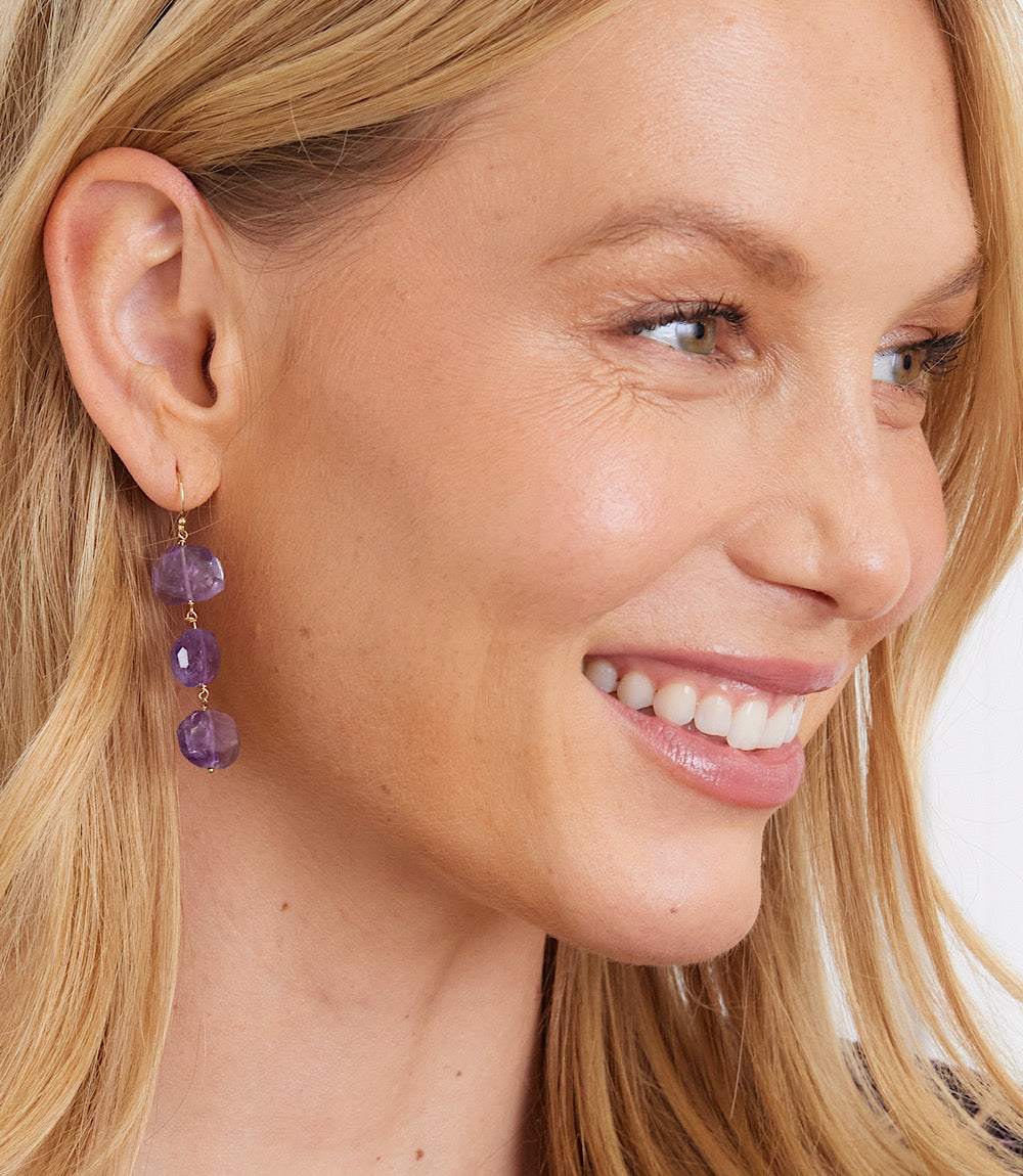 Close-up of a woman wearing 14k gold plated tiered amethyst gemstone earrings, 2.25 inches long