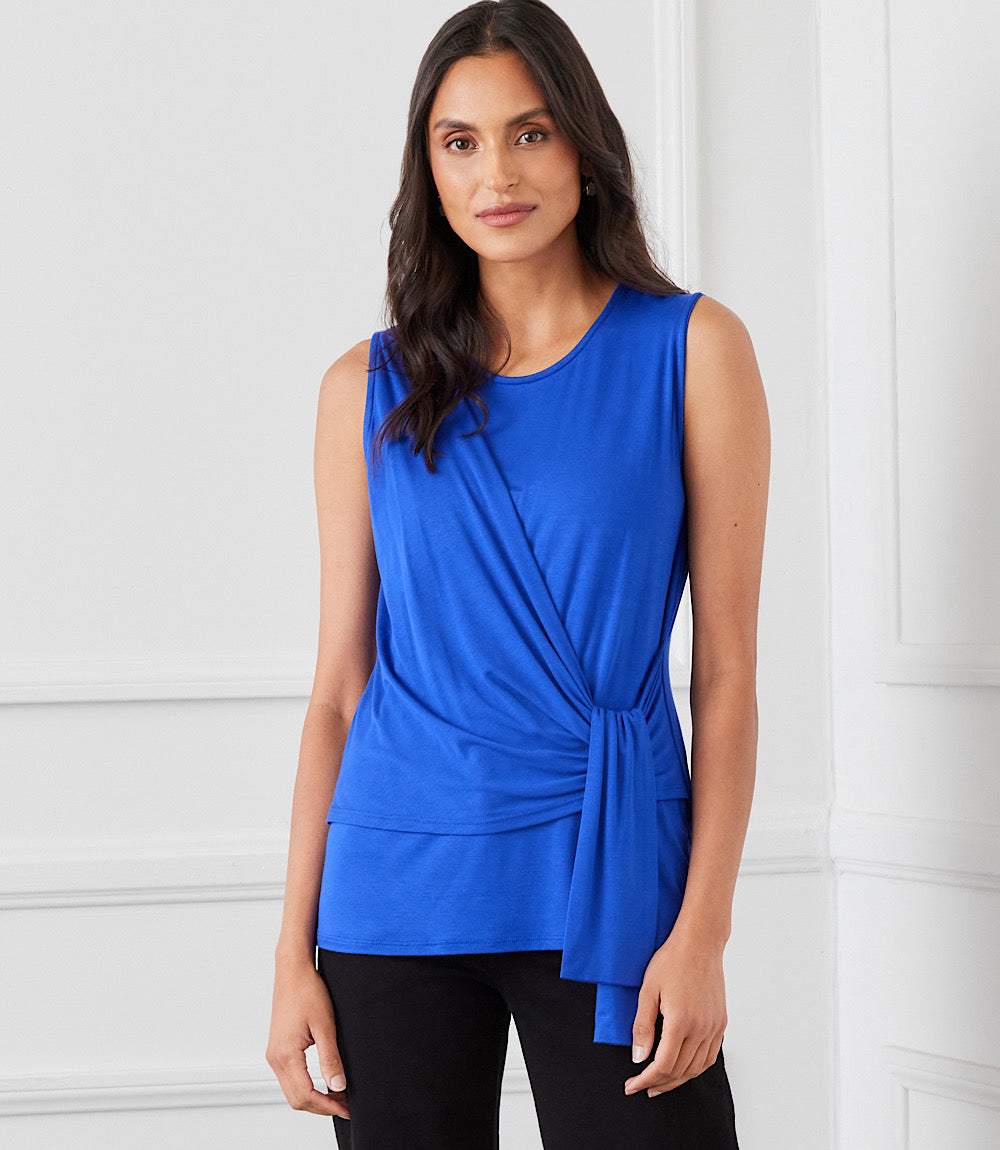 Woman wearing a sleeveless royal blue Side Drape Top with a side-tie detail and scoop neck.