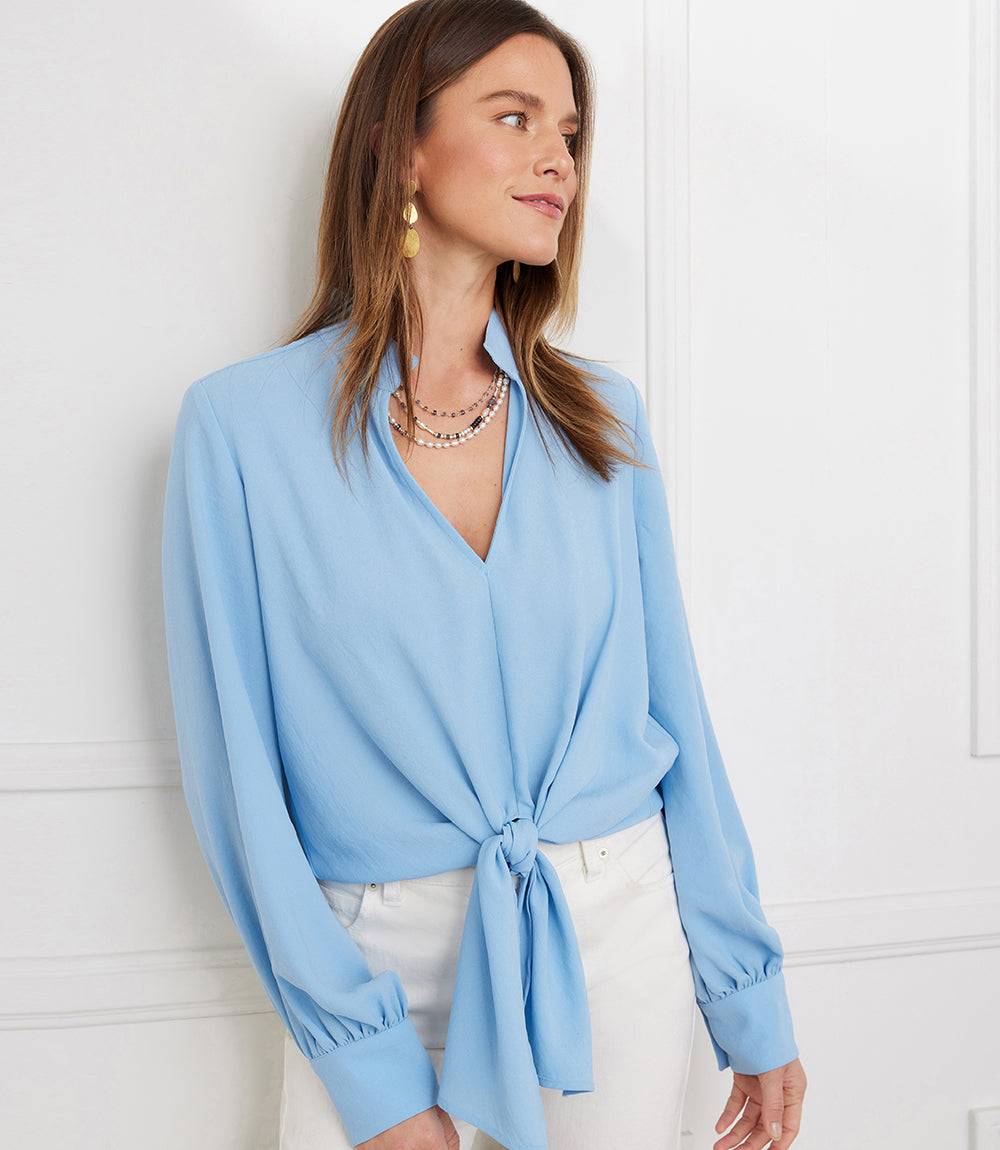 Woman wearing a light blue long sleeve tie-front top with mandarin collar paired with white pants
