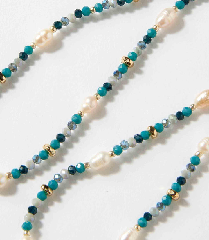 Close-up of a beaded gemstone and pearl stretch bracelet featuring mixed blue gemstones, pearls, and small gold accents on a stretch band