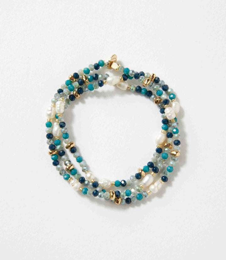 Beaded gemstone and pearl stretch bracelet with mixed blue and gold beads on white background