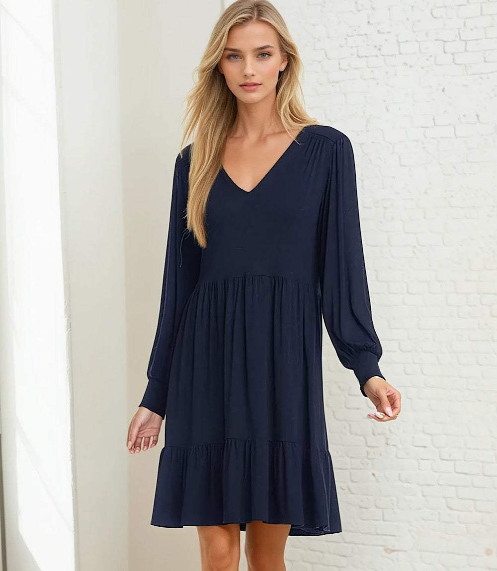 Woman wearing a navy long sleeve tiered dress with V-neckline and gathered cuffs, knee-length and flowy fit