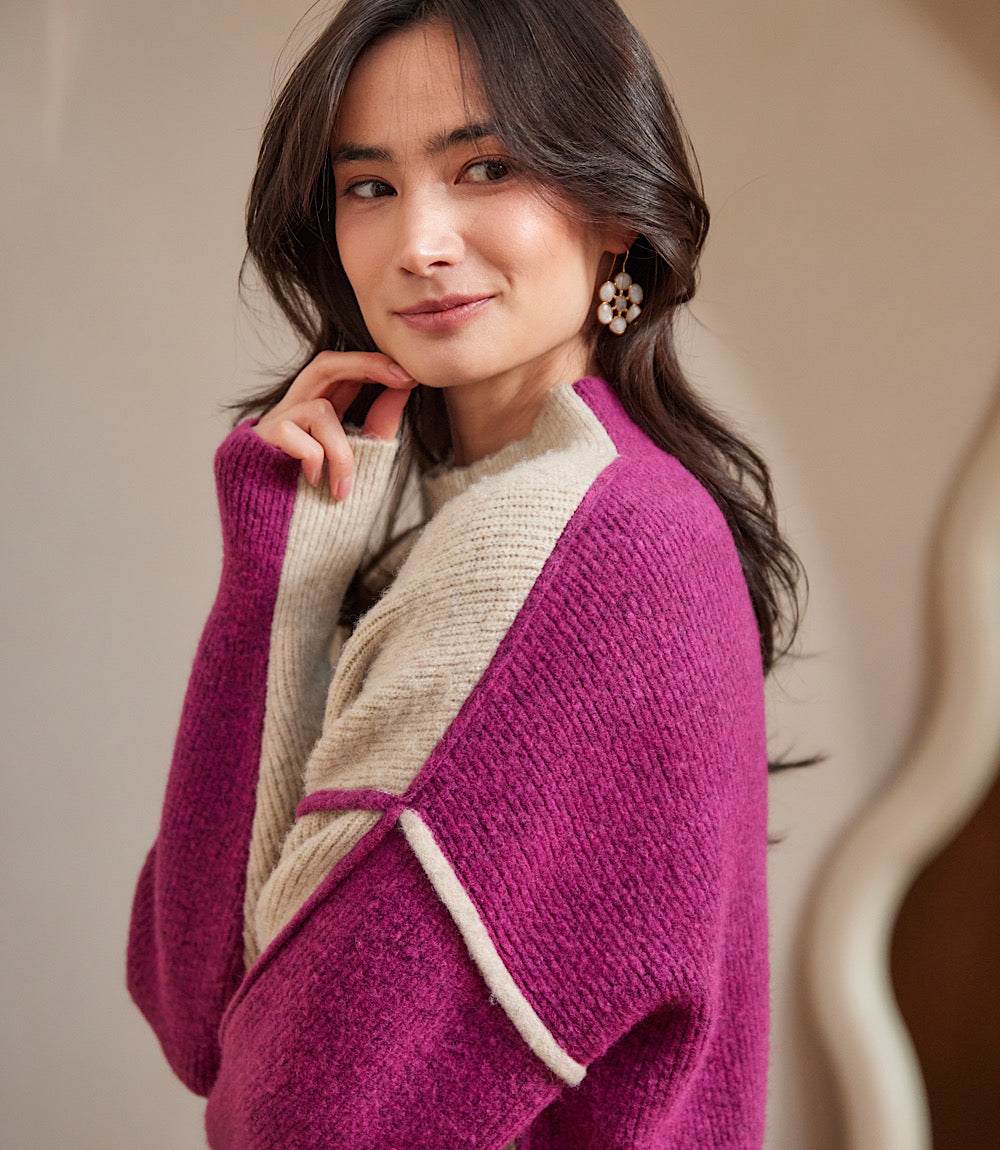 Woman wearing a relaxed fit colorblock mock neck sweater with purple and beige panels and exposed seam details