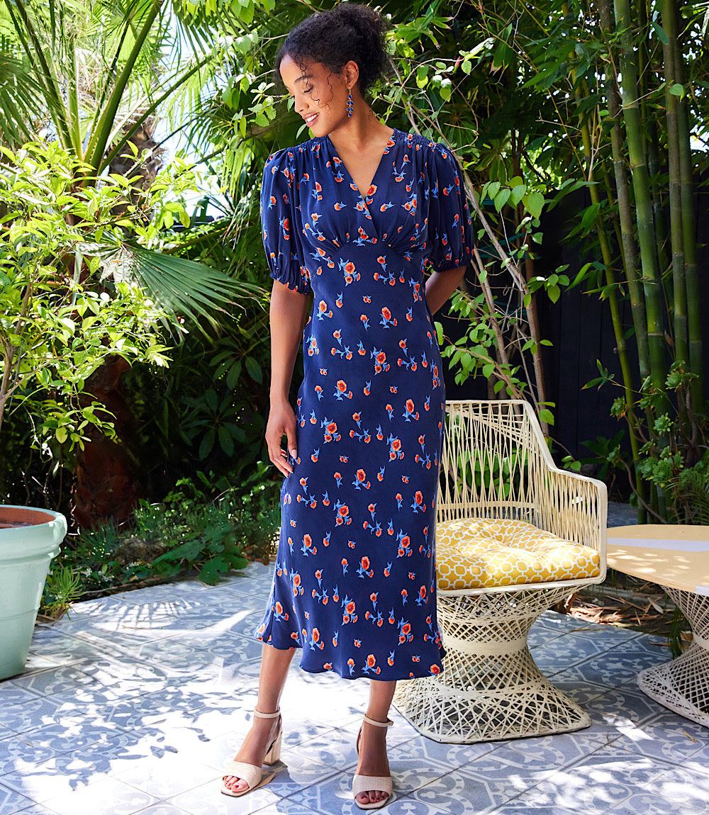 Woman wearing a navy bias puff sleeve dress with orange carnation print standing outdoors