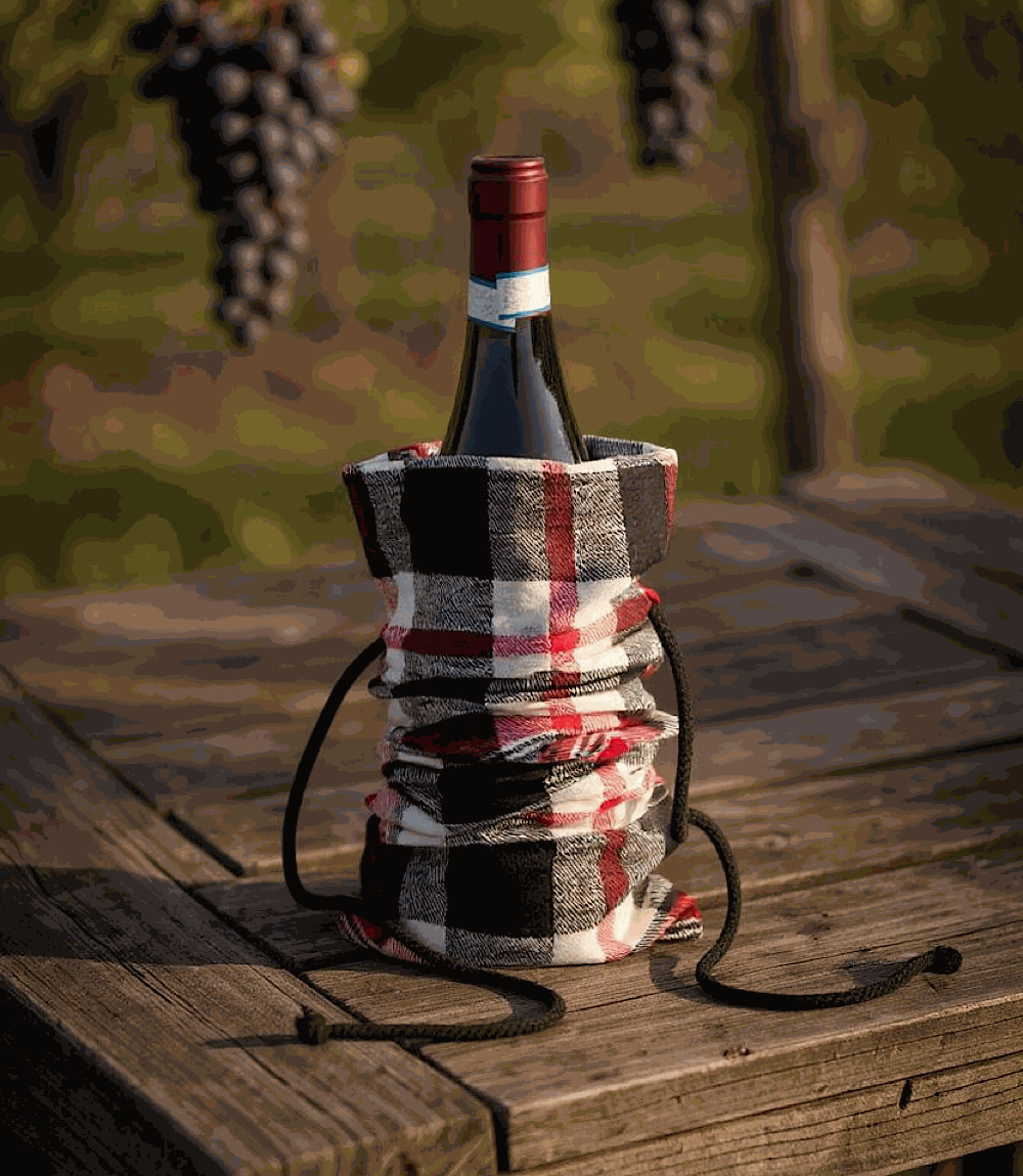 Plaid cotton wine bag with drawstring closure holding a wine bottle on a wooden table outdoors