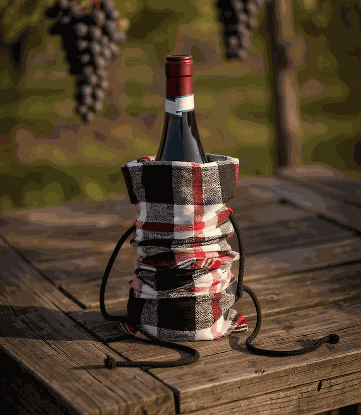 Plaid cotton wine bag with drawstring closure holding a wine bottle on a wooden table outdoors