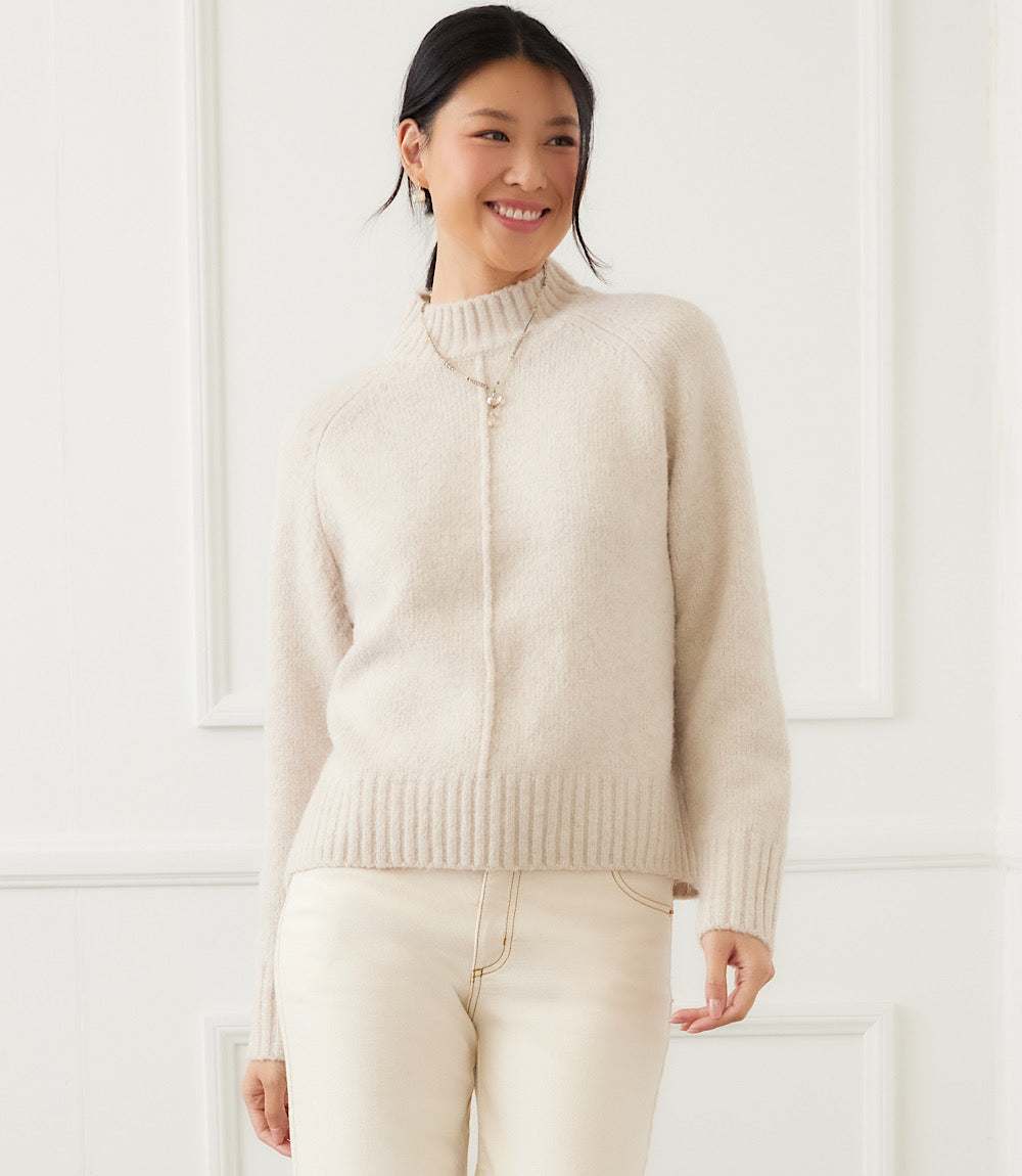 Woman wearing a soft beige turtleneck sweater with raglan sleeves and exposed center seam