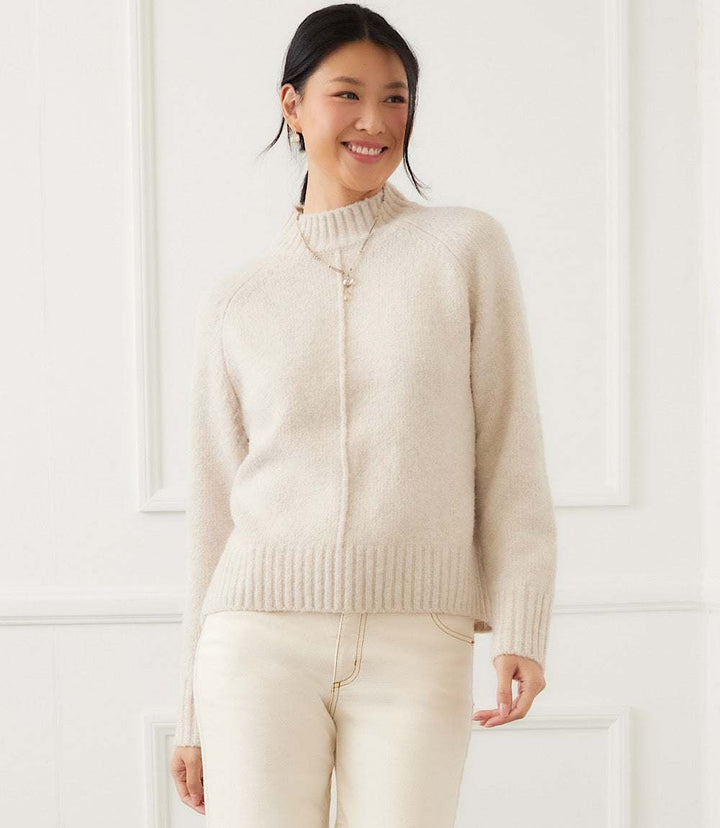 Woman wearing a soft beige turtleneck sweater with raglan sleeves and exposed center seam