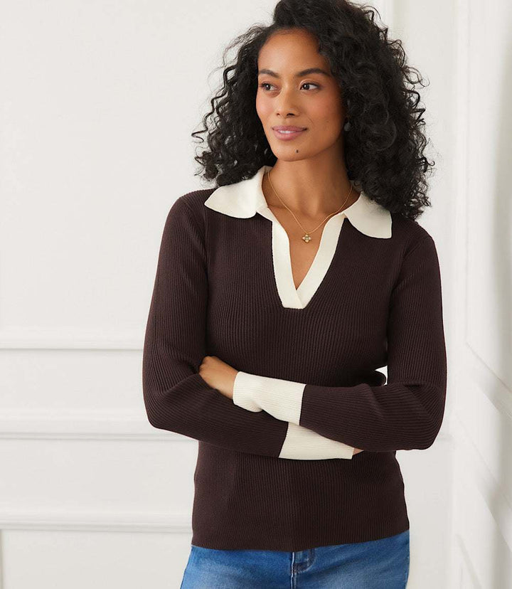 Woman wearing a contrast ribbed polo sweater with a white collar and cuffs, paired with blue jeans.