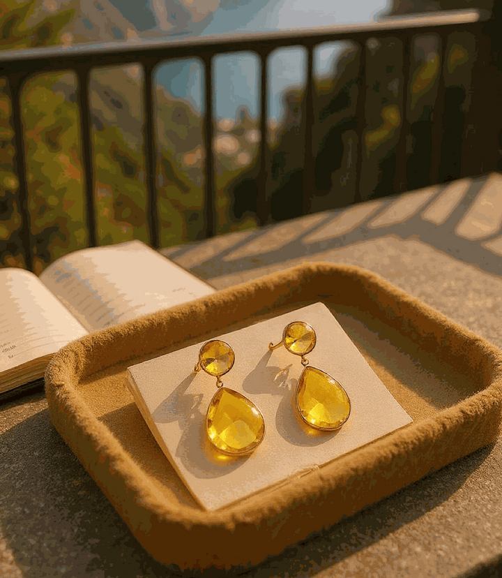 Teardrop gemstone citrine drop earrings with gold plating displayed on a velvet tray against a blurred outdoor background