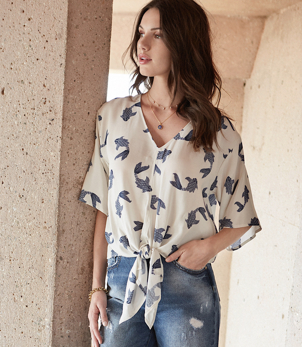 Woman wearing a white tie front top with blue butterfly koi print paired with denim jeans