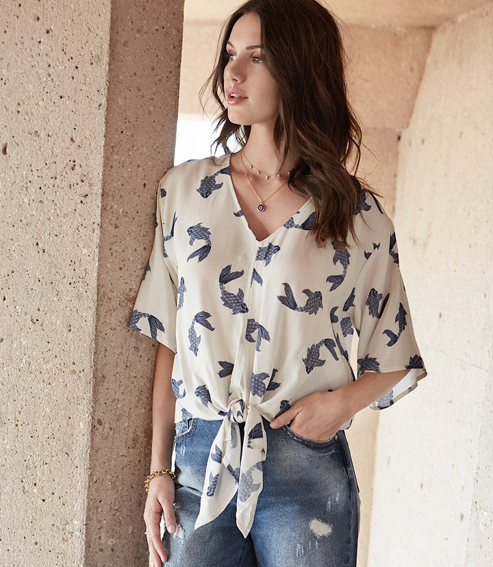 Woman wearing a white tie front top with blue butterfly koi print paired with denim jeans