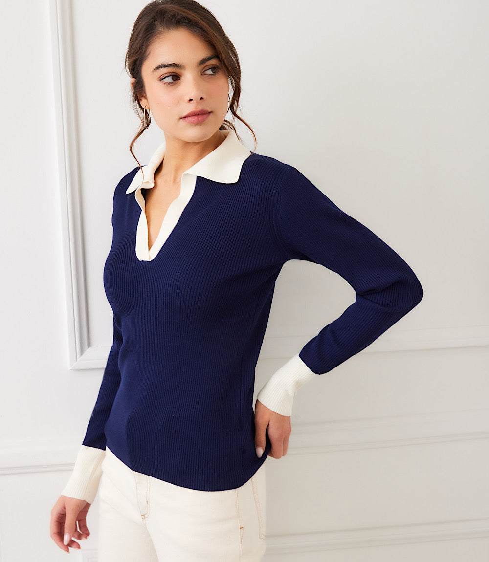 Woman wearing a navy contrast ribbed polo sweater with white collar and cuffs, paired with white pants.