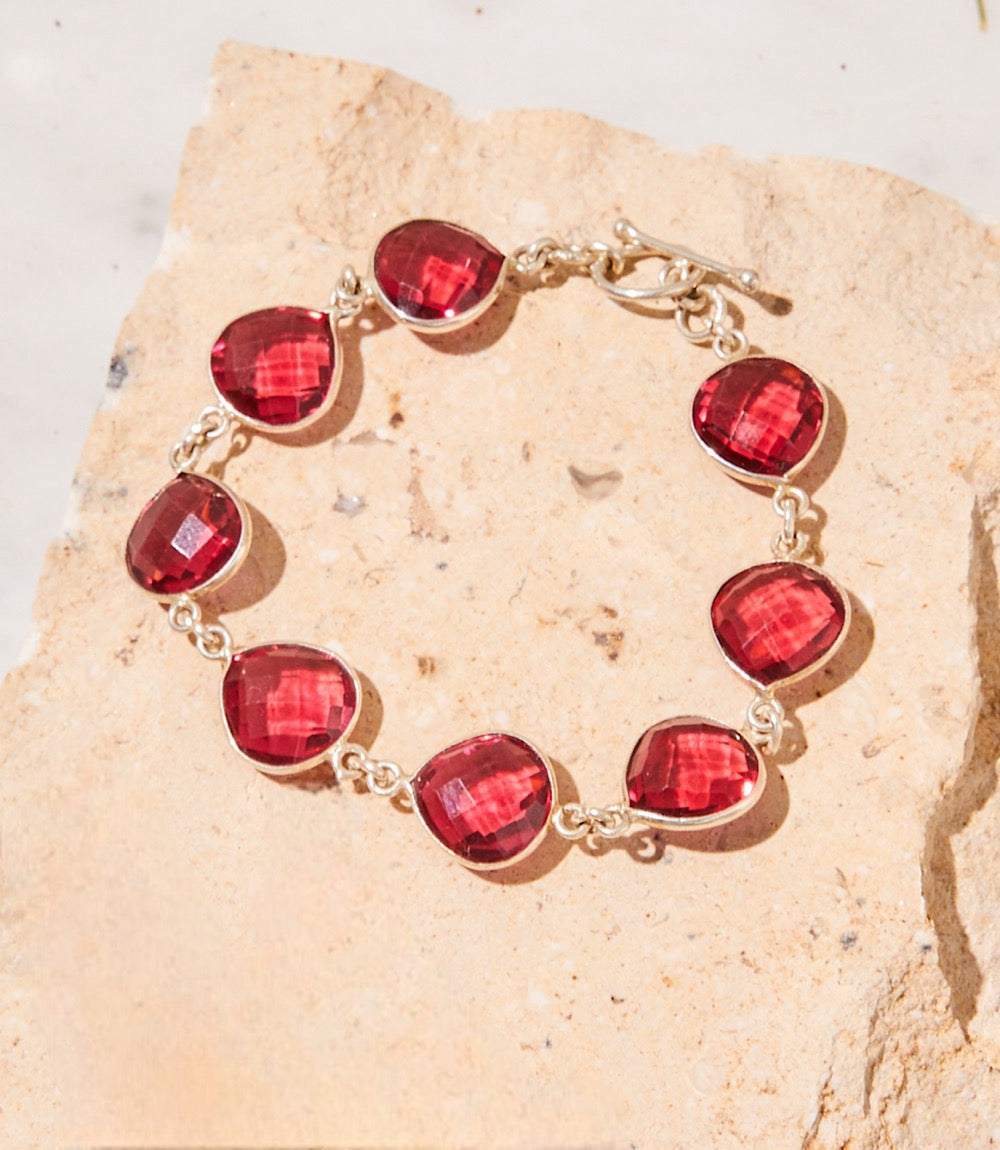 Dark pink amethyst quartz bracelet with faceted stones and silver links on a textured stone surface