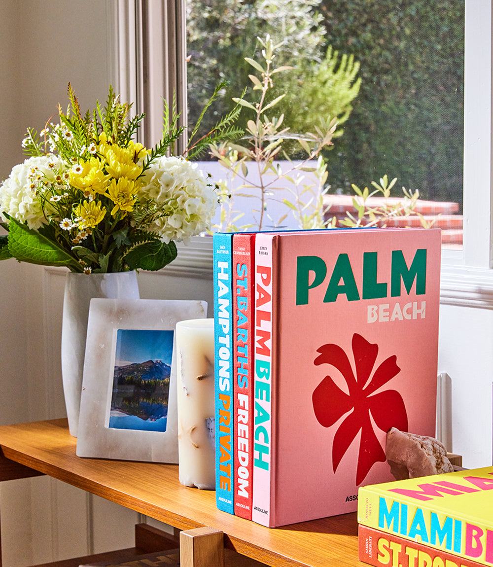 Palm Beach hardcover book by Aerin Lauder displayed on a wooden table next to flowers and candles.