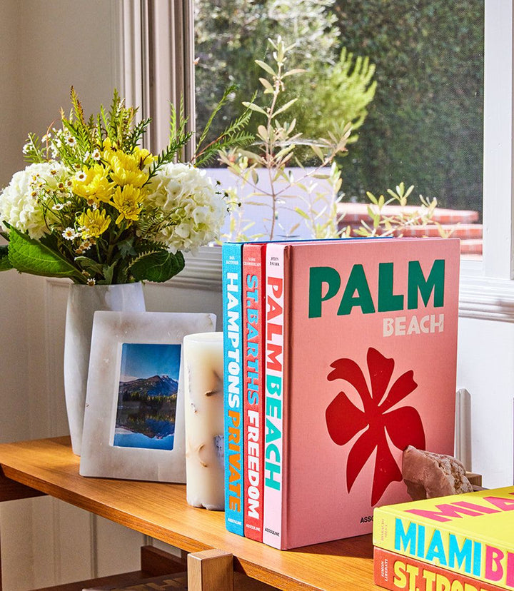 Palm Beach hardcover book by Aerin Lauder displayed on a wooden table next to flowers and candles.