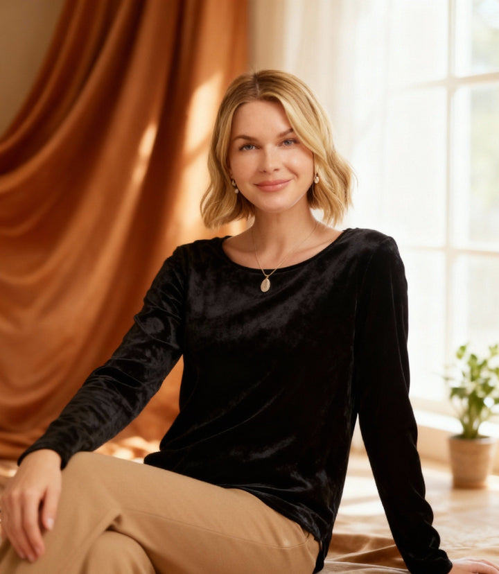 Woman wearing black long sleeve crushed velvet shirttail top sitting indoors