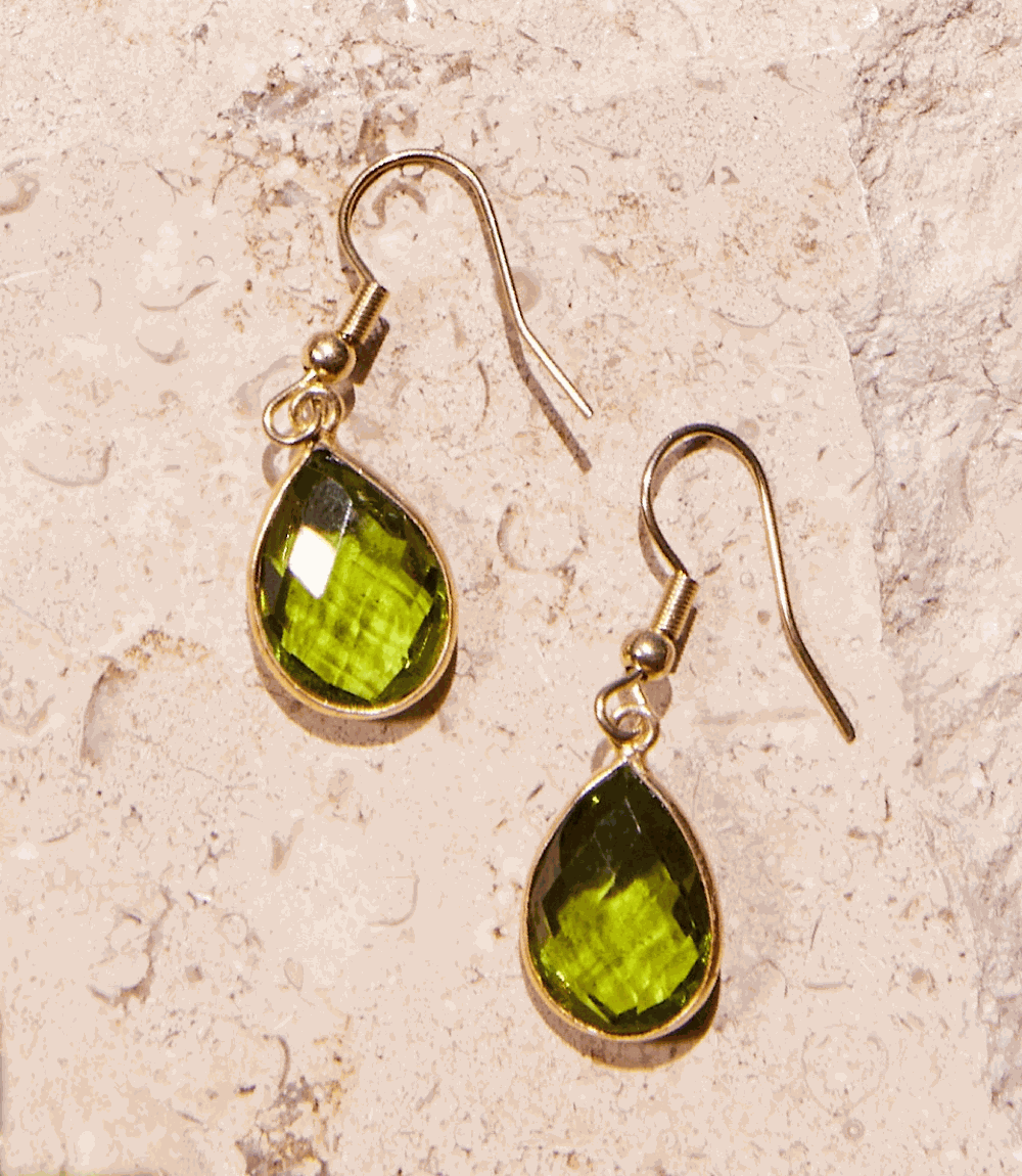 Peridot gemstone drop earrings with gold hooks on textured stone background