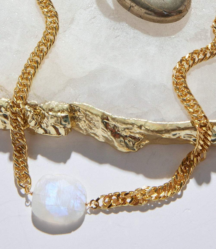 Moonstone pendant necklace with gold-tone chain and luminous white moonstone pendant on textured surface