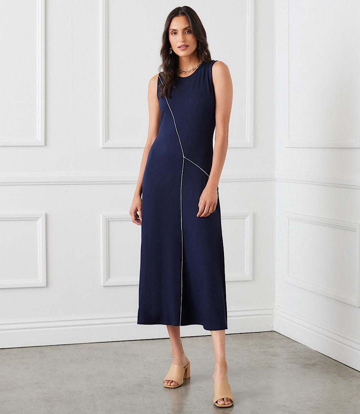 Woman wearing navy sleeveless reverse seam dress with scoop neck and midi length