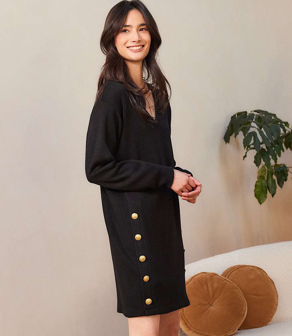Woman wearing black long sleeve V-neck dress with gold-tone button details on sides