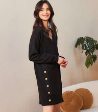 Woman wearing black long sleeve V-neck sweater dress with gold button details on the sides