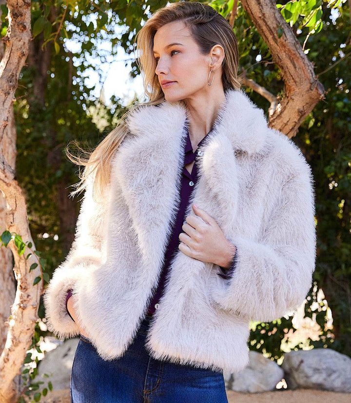 Woman wearing a cropped cream faux fur jacket with wide notched collar and button front closure outdoors