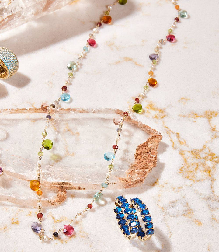Long beaded gemstone necklace with multicolored semiprecious stones and 14k gold vermeil on a marble surface with blue gemstone earrings