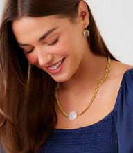 Woman wearing gold-tone moonstone pendant necklace with matching earrings and blue top