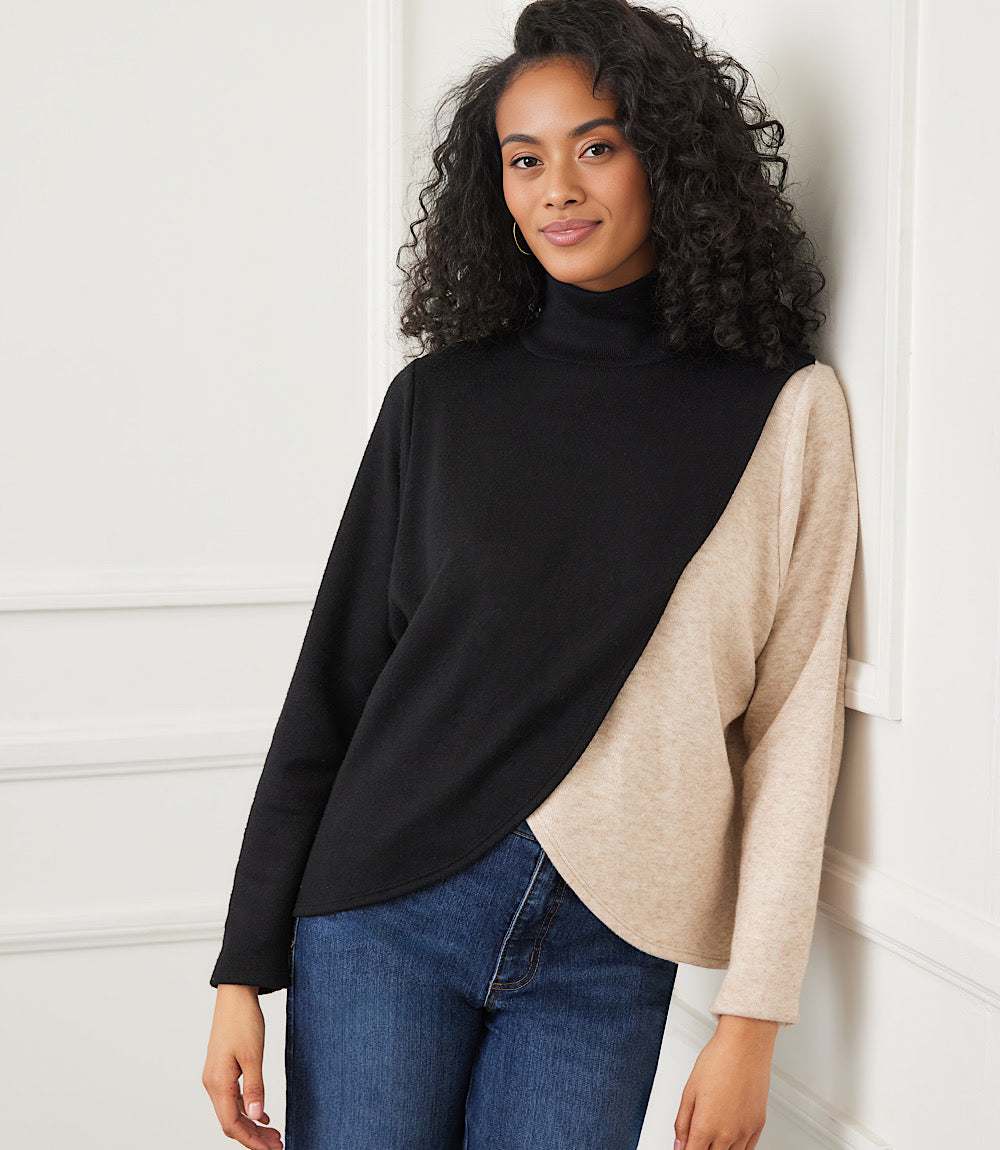 Woman wearing a long sleeve crossover colorblock top with mock neck and curved hemline in black and beige.