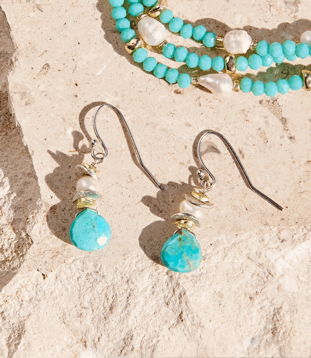 Turquoise dangle earrings with sterling silver hooks, turquoise stones, freshwater pearls, and gold accents on a stone background.