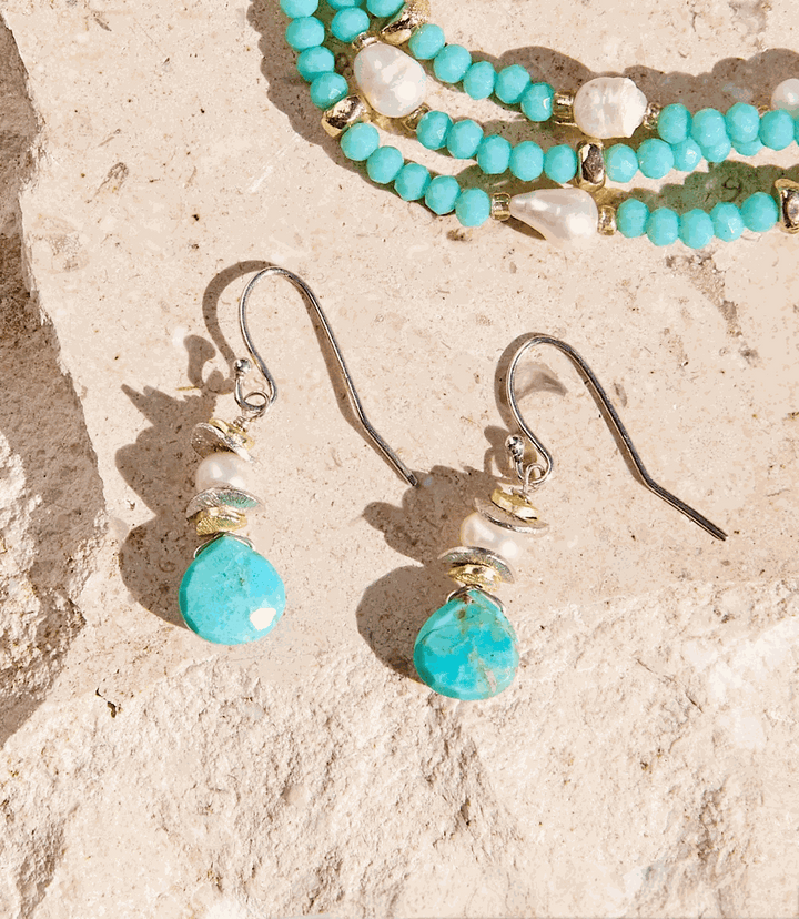 Turquoise dangle earrings with sterling silver hooks, turquoise stones, freshwater pearls, and gold accents on a stone background.