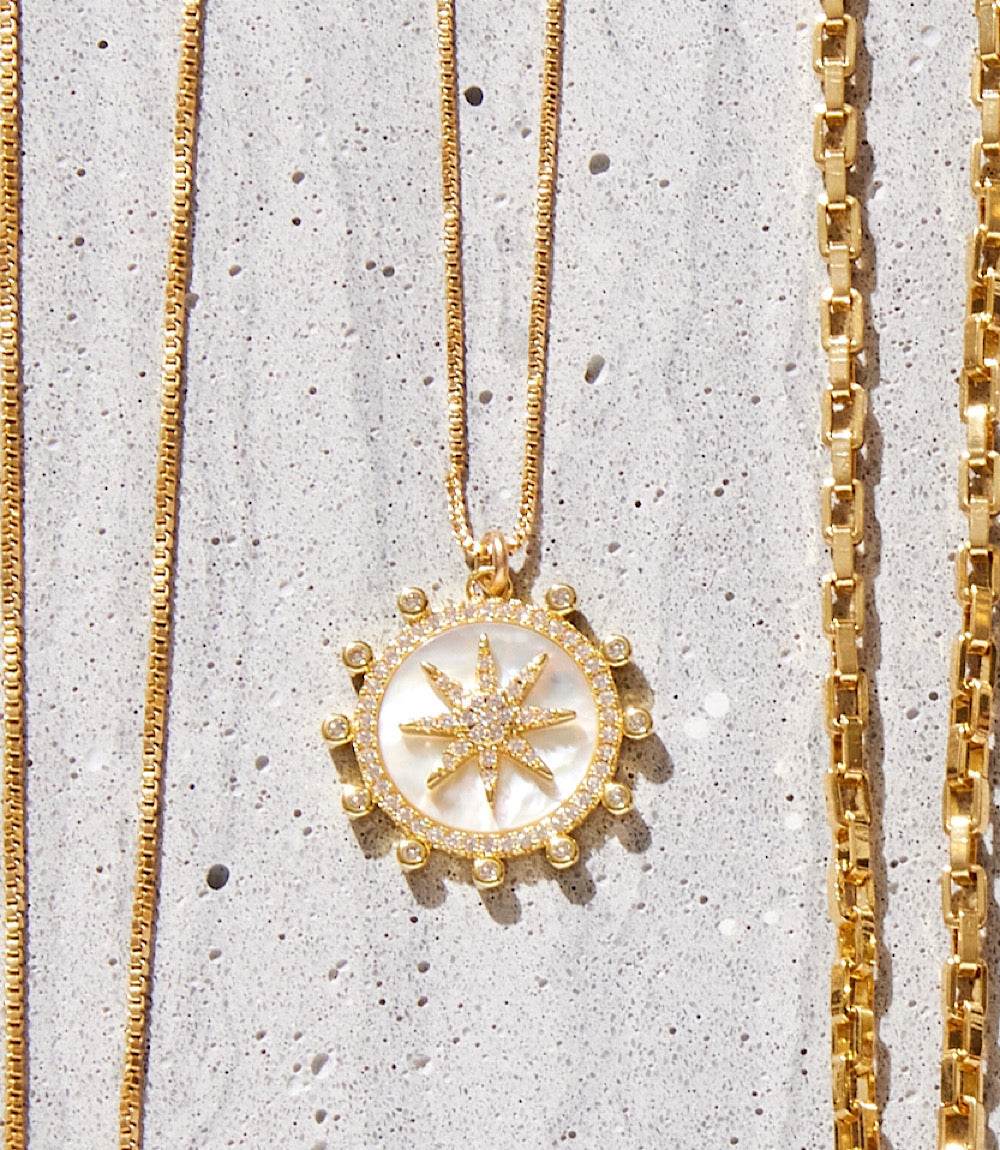18k gold fill Starburst Charm Necklace with micro pave cubic zirconia pendant on a delicate chain on textured background