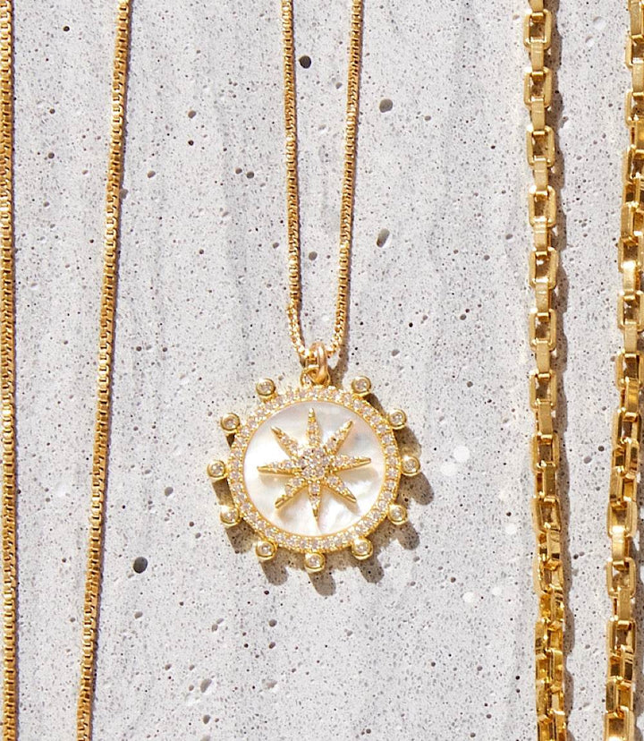 18k gold fill Starburst Charm Necklace with micro pave cubic zirconia pendant on a delicate chain on textured background
