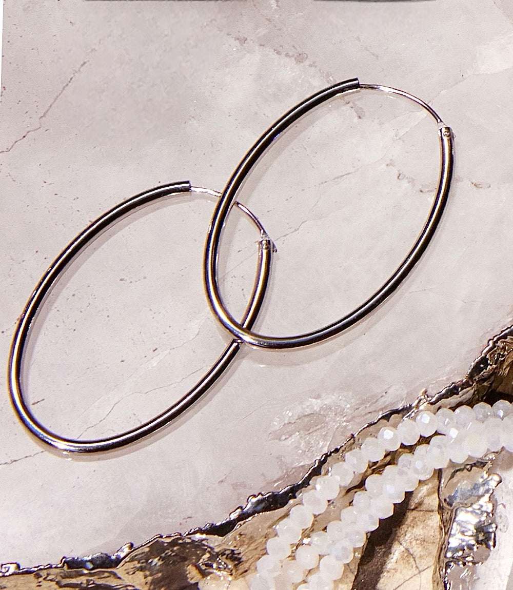 Pair of elegant 925 sterling silver oval hoop earrings on a marble surface next to white beaded jewelry