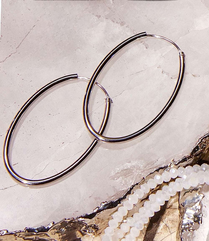 Pair of elegant 925 sterling silver oval hoop earrings on a marble surface next to white beaded jewelry