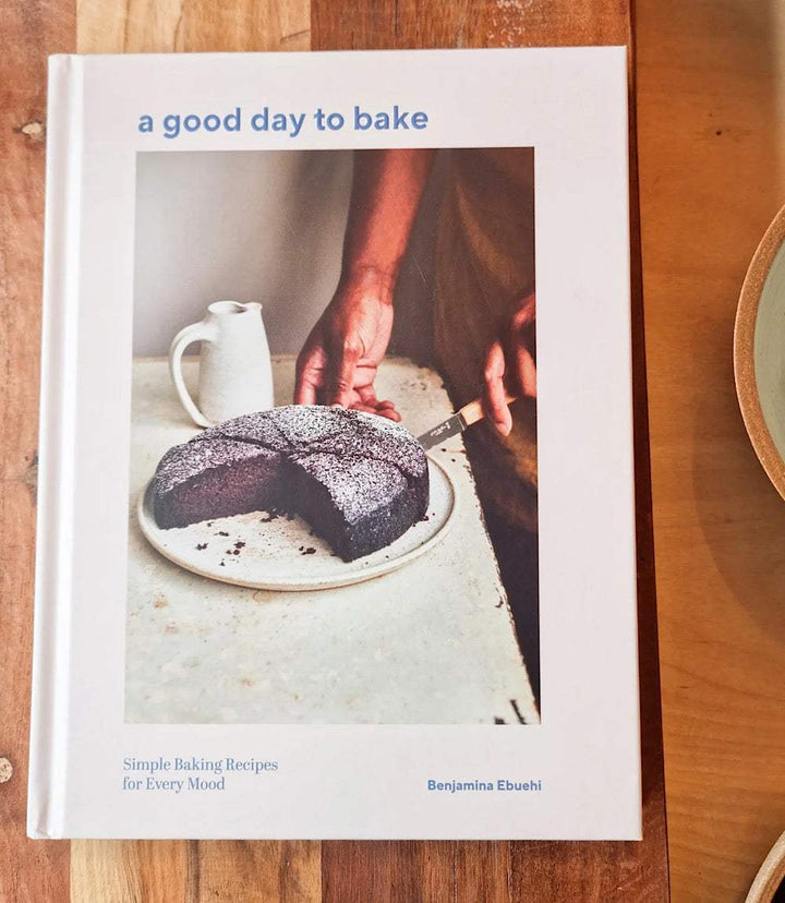 Cover of cookbook "A Good Day To Bake" by Benjamina Ebuehi featuring a chocolate cake and simple baking scene