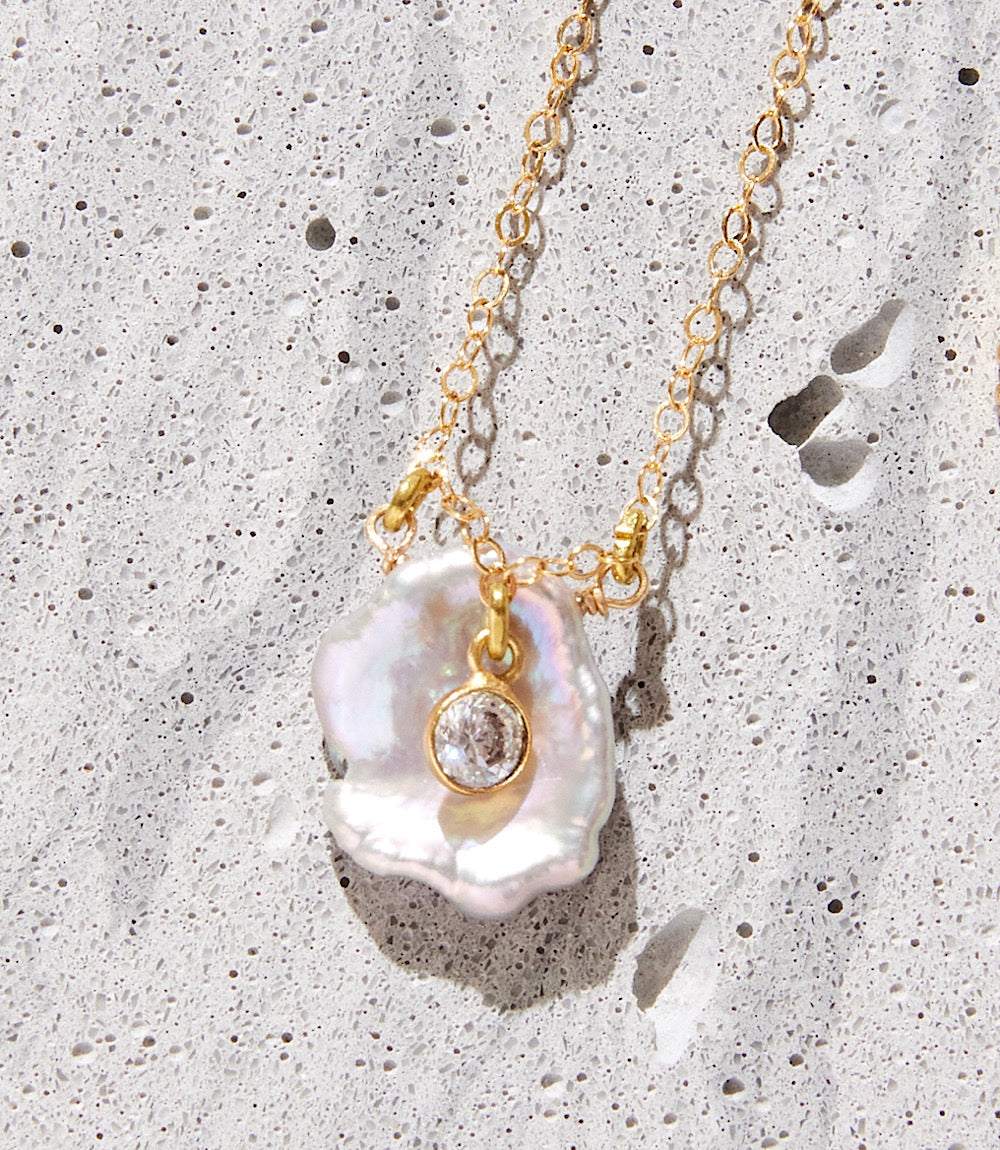 Crystal pearl necklace with 14k gold-fill, purple freshwater Keishi pearl, and cubic zirconia pendant on textured background