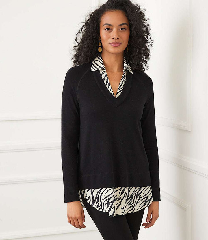 Woman wearing layered contrast zebra sweater with black V-neck top and zebra print collar and hem detail