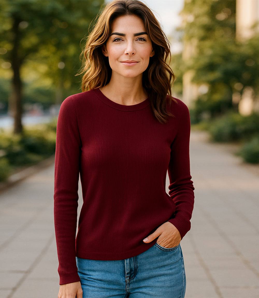 Woman wearing a fitted long sleeve ribbed crewneck top in burgundy paired with blue jeans outdoors