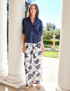Woman wearing a navy shirt and floral pants standing in a garden setting.