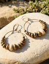Beaded earrings on a stone surface with greenery in the background